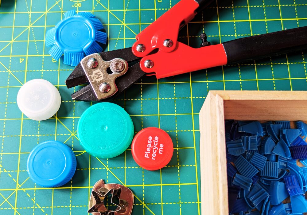 Plastic bottle tops with bolt cutters and cookie cutters on a workmat