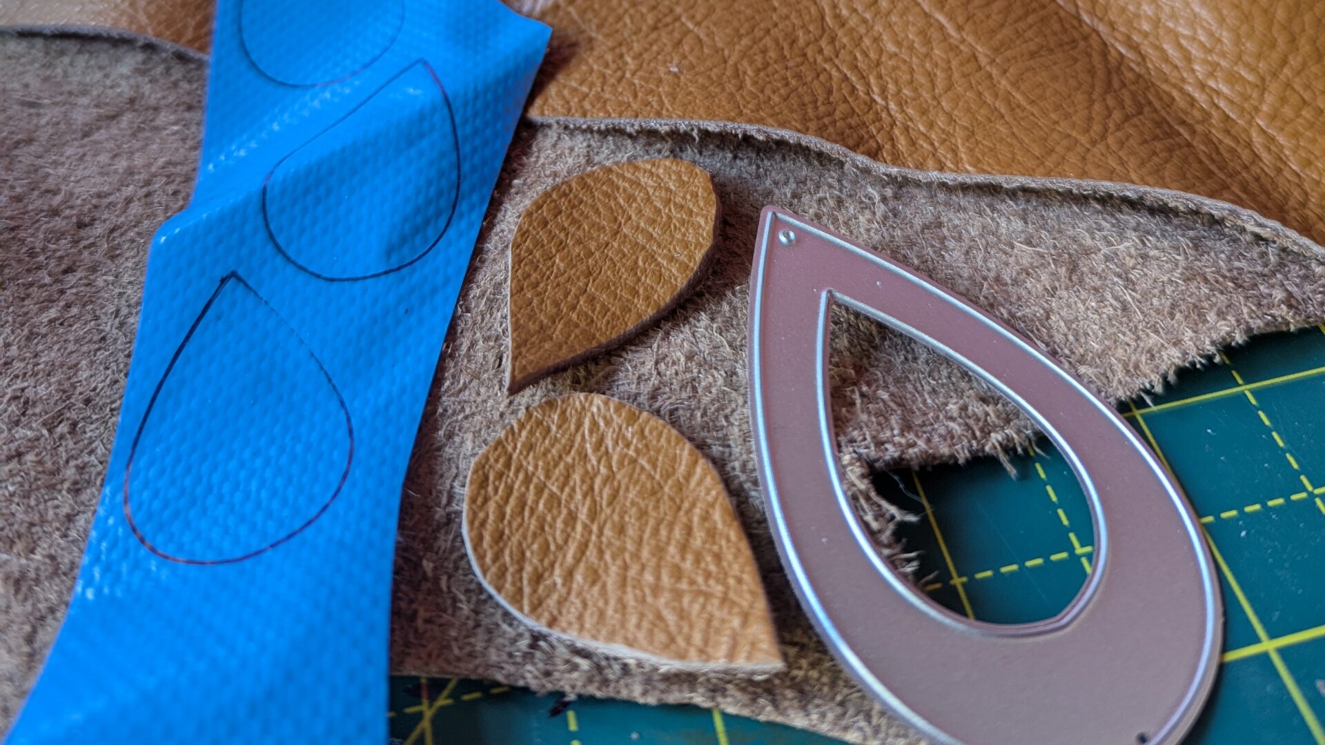 Leather and other fabrics on a cutting table with templates and cutouts of teardrop shapes.