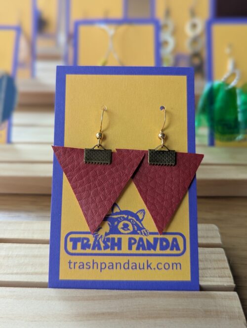 A close up photo of a pair of dangly earrings on a display card. Red leather earrings with brass fixtures