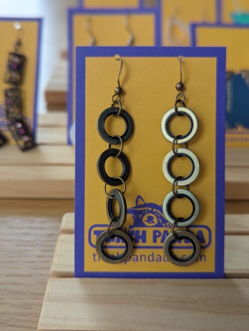 A close up photo of a pair of brass and rubber recycled earrings on a jewellery display card