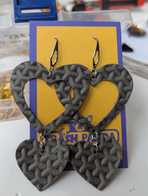 A pair of earrings - in grey basket-weave leather hearts - on a jewellery display card