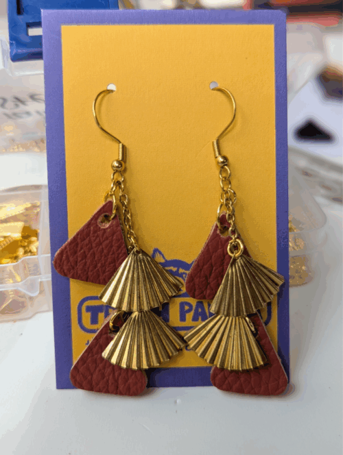 A pair of dangly earrings made with red leather and brass-multi-drop, on a brightly coloured earring display card