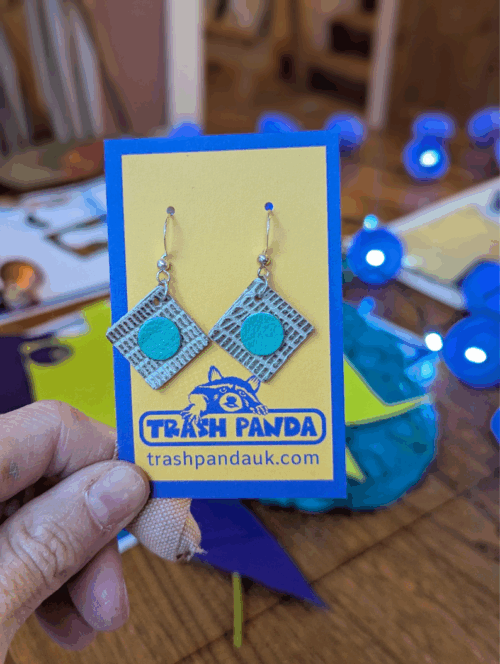 Dangly earrings made from upcycled leather offcuts. On a jewellery display card and held by a hand