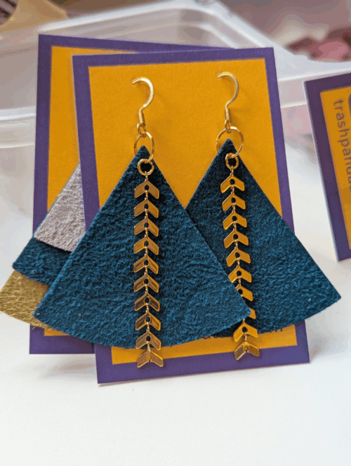 A pair of teal coloured triangle earrings sit on a jewellery display card. They are adorned with gold-coloured metal