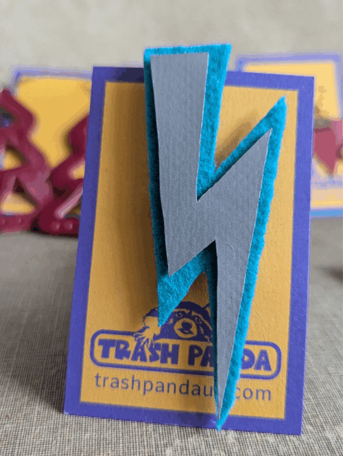 Upcycled lightning bolt brooch made from electric blue felt and a silver inflatable offcut, displayed on a Trash Panda backing card